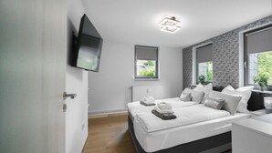 A modern bedroom with a bed, bedside tables, a TV mounted on the wall, and a window with a view of greenery. - Relaxing time-out on approx. 100sqm in an idyllic location with a large covered terrace (Jühnde)