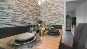 A dining area with a wooden table set for four, a stone-patterned wall, and a hanging light fixture. - Relaxing time-out on approx. 100sqm in an idyllic location with a large covered terrace (Jühnde)