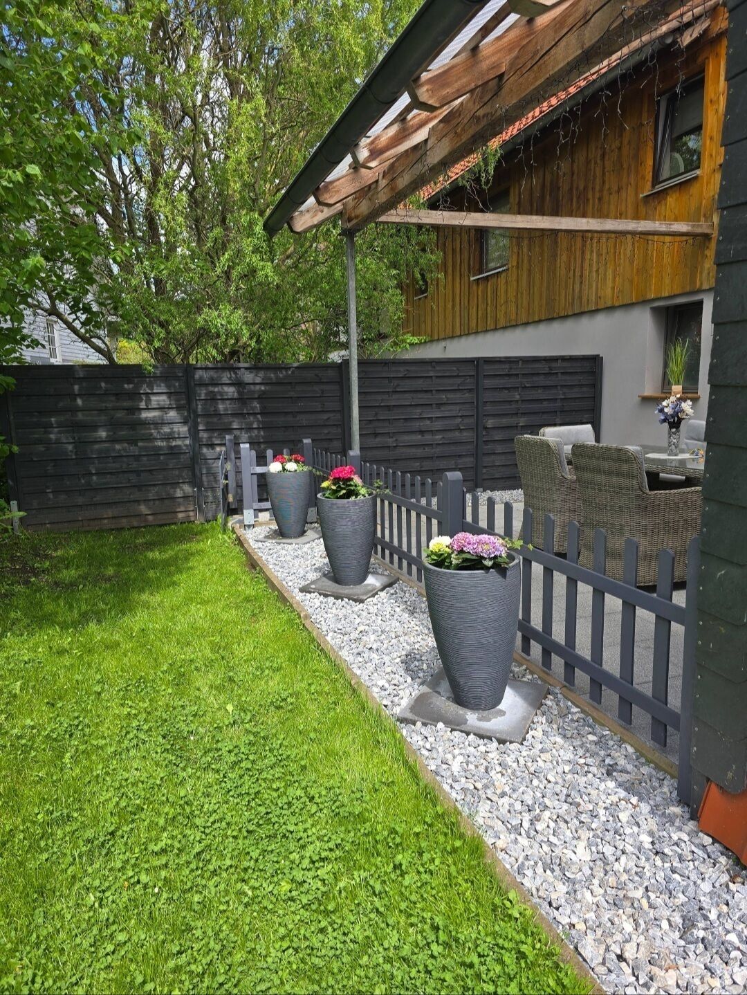 Un patio trasero con una terraza de madera, un pérgola y una zona de estar con una mesa y sillas.