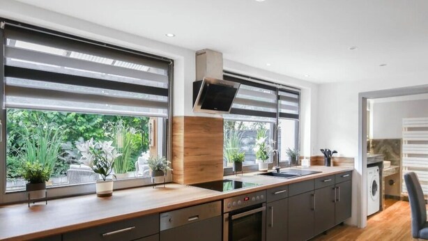 A modern kitchen with a built-in oven, a dishwasher, and a large window with blinds. - Relaxing time-out on approx. 100sqm in an idyllic location with a large covered terrace (Jühnde)