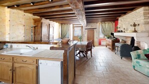 A kitchen with wooden cabinets, a dishwasher, a dining area with a table and chairs, a fireplace, and a stone wall. - Holiday Home 'Chez Pauline' with Private Garden (Massangis)