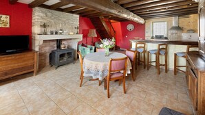 A dining area with a round table, chairs, a fireplace, a television, and a kitchen area with a sink and counter. - Holiday Home 'Chez Pauline' with Private Garden (Massangis)