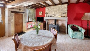 A dining area with a table set for two, a television, a fireplace, and a cozy armchair. - Holiday Home 'Chez Pauline' with Private Garden (Massangis)