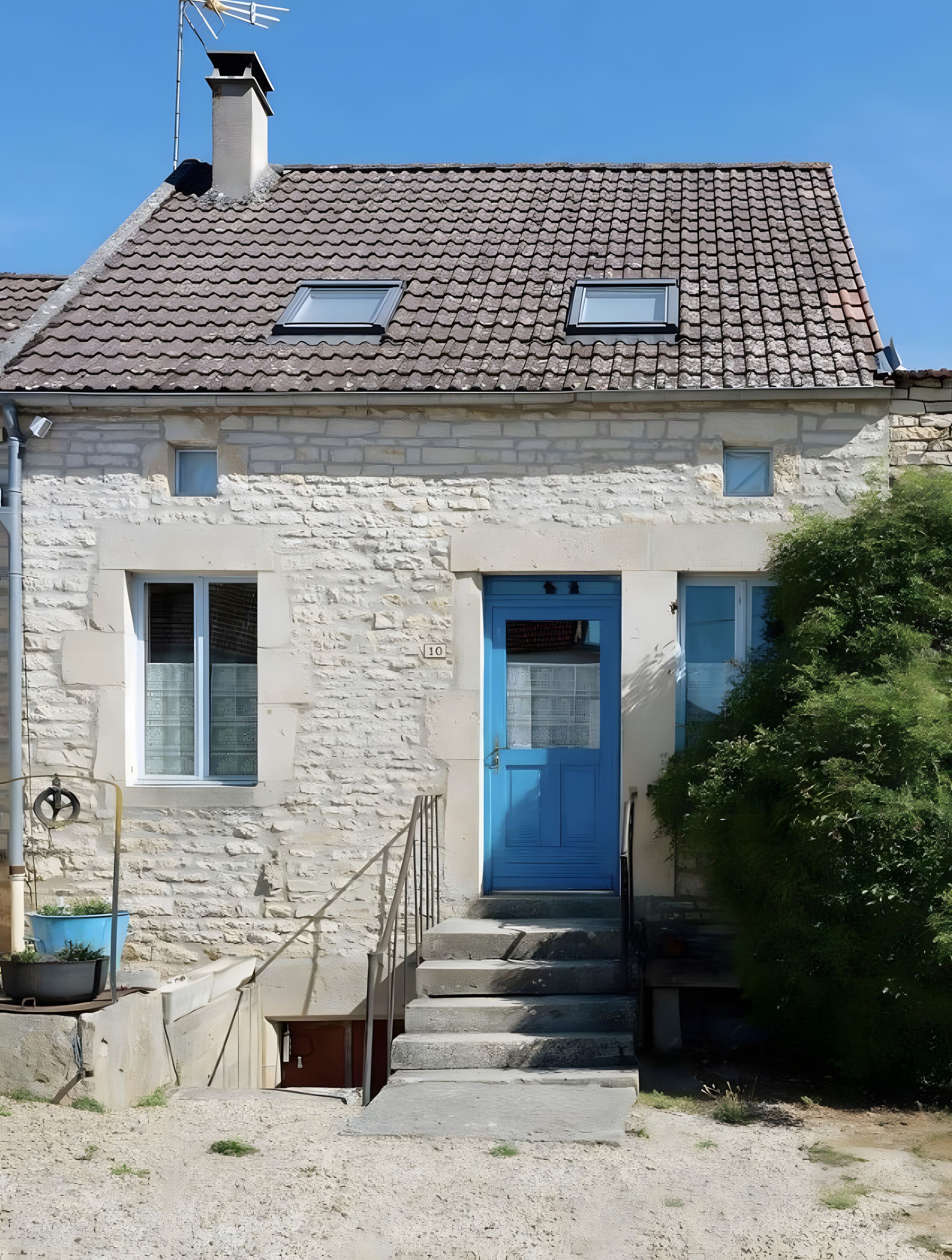 Ein Steinhaus mit einer blauen Tür, einem kleinen Fenster und einem Schornstein.