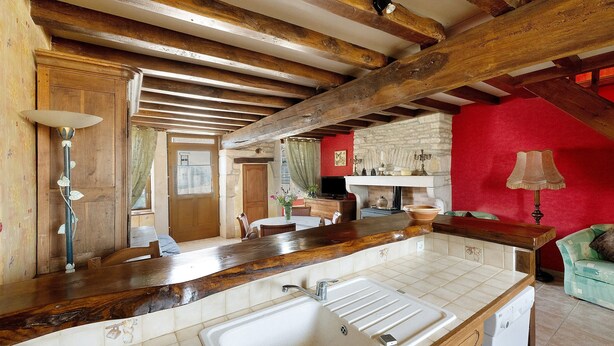A kitchen with a large sink, wooden beams, a red wall, and a dining area with a table and chairs. - Holiday Home 'Chez Pauline' with Private Garden (Massangis)