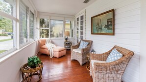 Habitación iluminada por el sol con muebles de mimbre, un cuadro y vistas al exterior.