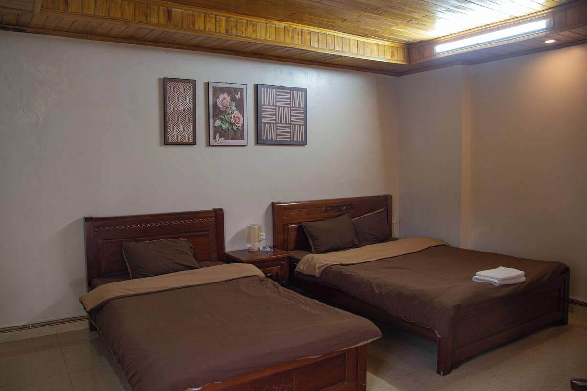 A bedroom with two wooden beds, a nightstand with a lamp, and two wall-mounted artworks.