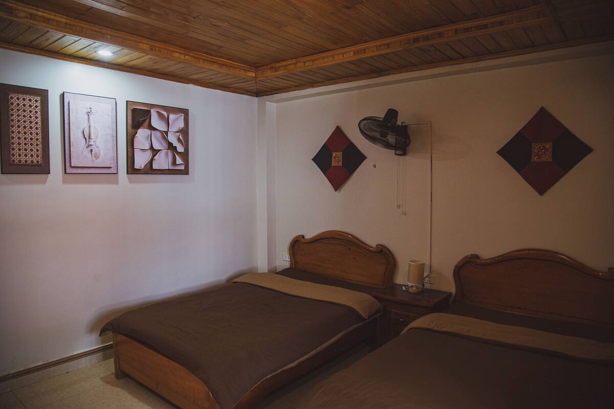 A room with two wooden beds, a ceiling fan, and three framed artworks on the wall.