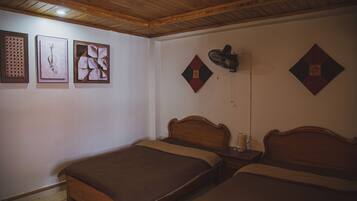 Una habitación con dos camas de madera, un ventilador de techo y tres obras de arte enmarcadas en la pared.
