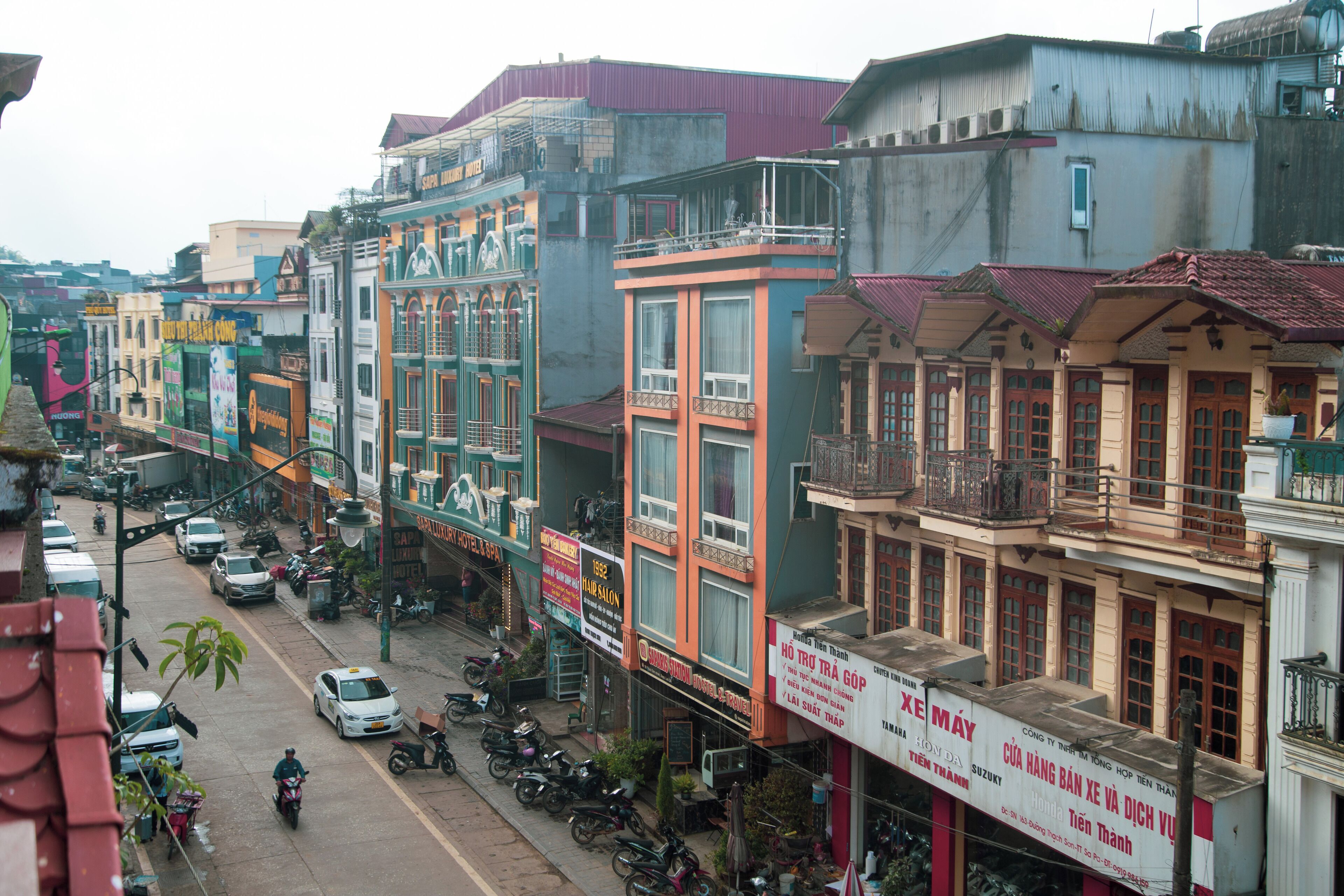 A street view with buildings, parked motorcycles, and cars.