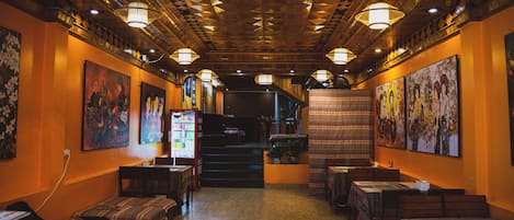 A restaurant interior with wooden ceiling, tables, chairs, and wall-mounted artwork.