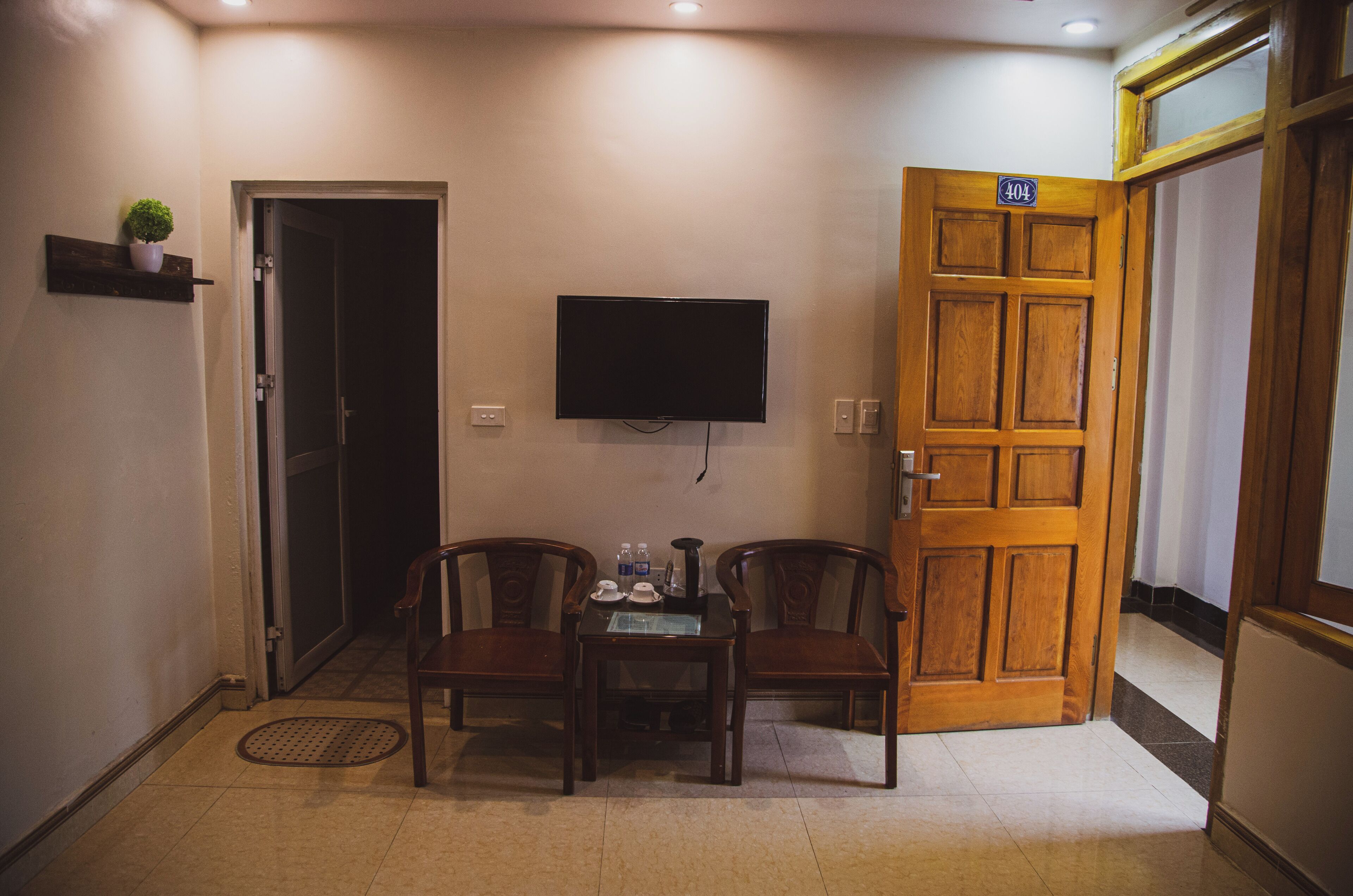 A hotel room with a wooden door, a television mounted on the wall, and a small table with two chairs.