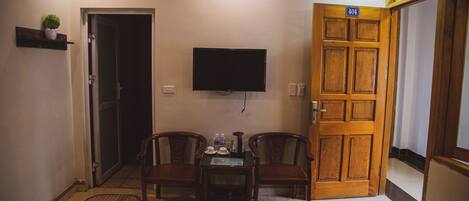 A hotel room with a wooden door, a television mounted on the wall, and a small table with two chairs.