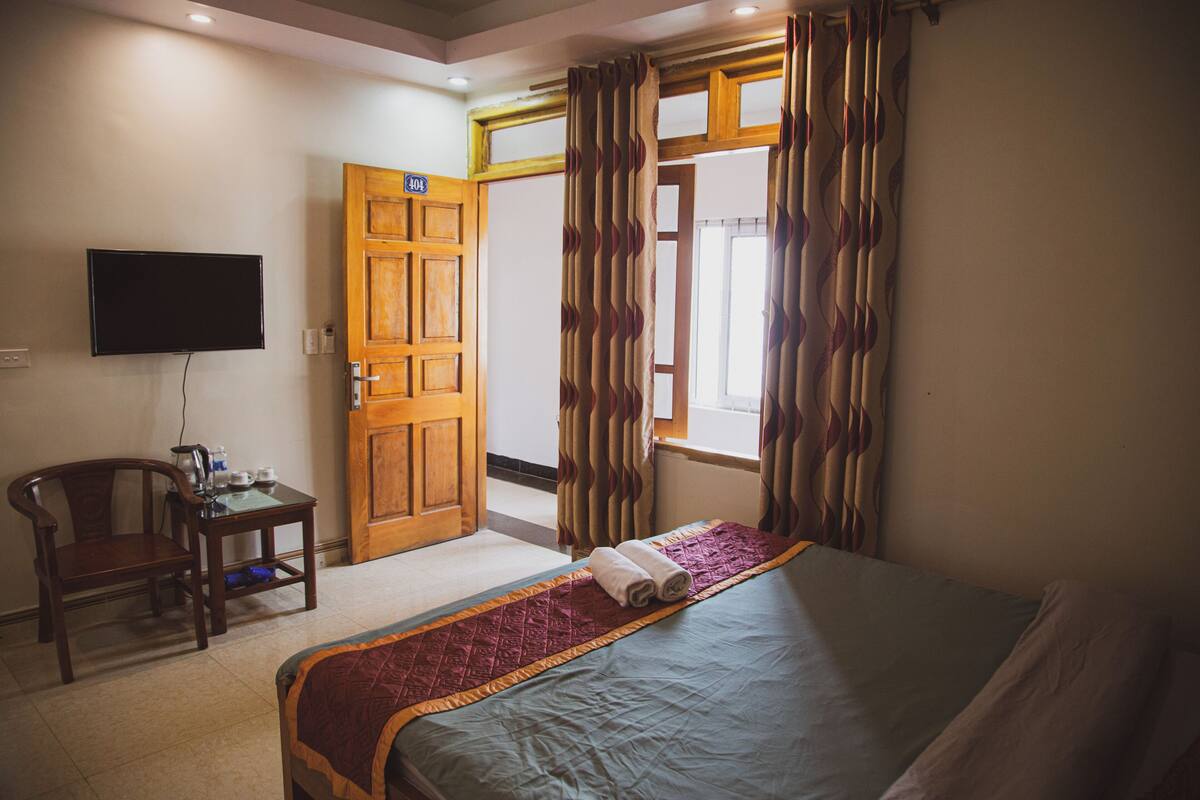A hotel room with a bed, a desk with a chair, a television, and a door leading to another room.