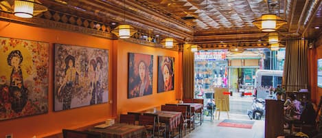 An interior with wooden ceiling, tables, chairs, and artwork on the walls.
