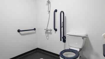 A bathroom with a white toilet, black floor, and white walls. There are grab bars on the wall and a trash can.