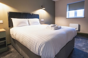 A neatly made bed with white linens, a headboard, and a bedside table with a lamp. - Pairc House Hotel (Birmingham)