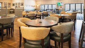 A spacious dining area with multiple tables and chairs, framed pictures on the walls, and a large window providing natural light. - Pairc House Hotel (Birmingham)