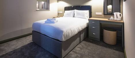 A modern hotel room with a large bed, a desk, and a small window.
