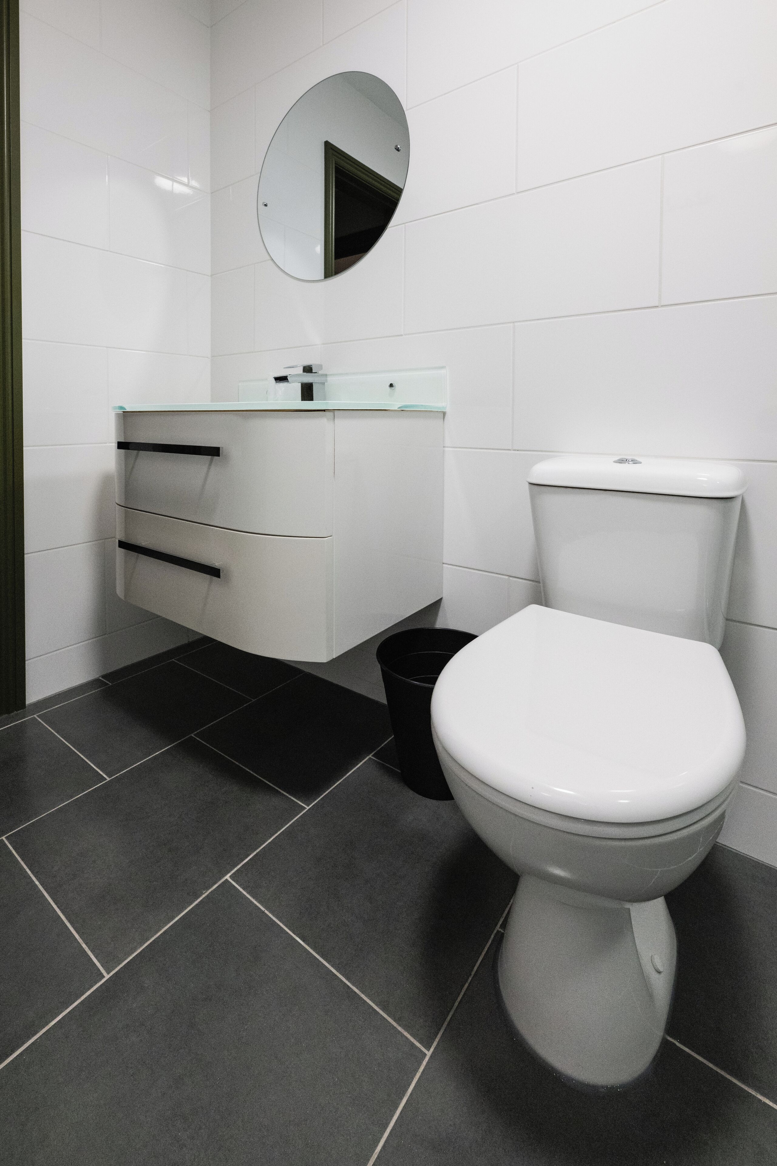 A modern bathroom with a white toilet, a glass sink, and a black trash bin.