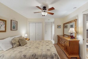 A bedroom with a bed, a ceiling fan, a dresser, a mirror, and a door leading to another room. - Scenic-view cottage with sunroom, deck, kitchen & pool - close to beach & golf (Kiawah Island)