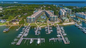 An aerial view of a marina with multiple docks and boats, surrounded by hotels with a central pool area.