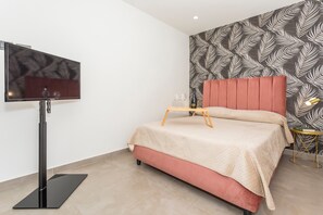 A modern bedroom with a flat-screen TV, a bed with a red headboard, a patterned wall, and a small side table.