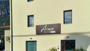 A building with a sign reading 'Aima Boutique Rooms' and a door with a glass panel. There are two potted plants on the sidewalk.