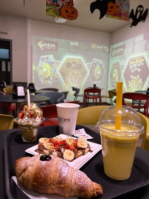 Un plateau contenant un dessert, une boisson et une pâtisserie, placé dans un espace de restauration où un écran de projection est visible à l'arrière-plan.