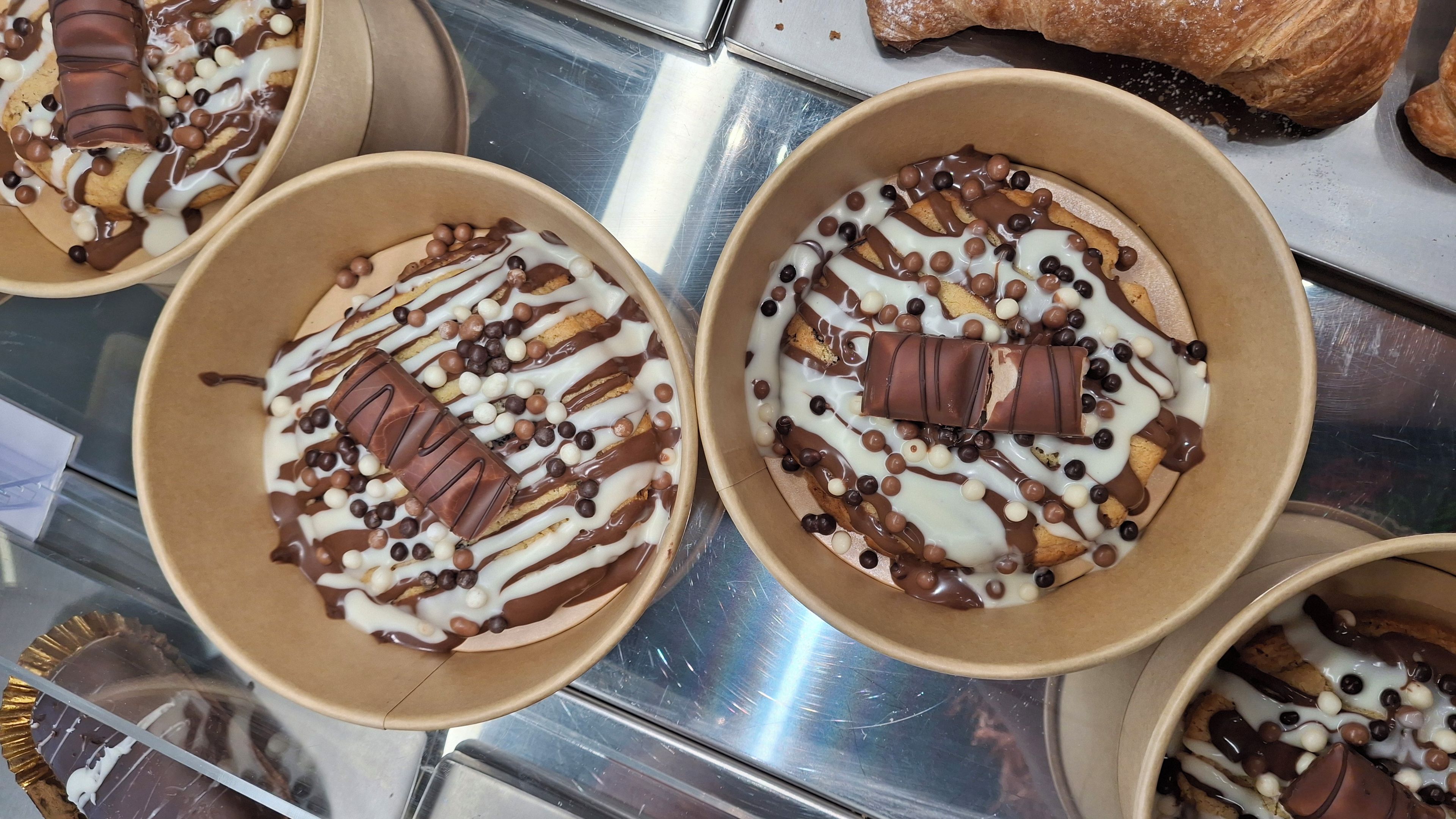 Mostra de postres amb diversos bols que contenen un postre en capes cobert amb regirat d'ametlla i xocolata blanca, trossos de xocolata i caramels rodons.