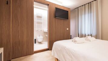 Una habitación de hotel con un armario de madera, un televisor de pantalla plana, una cama con ropa blanca y un baño con lavabo e inodoro.