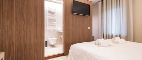 A hotel room with a wooden wardrobe, a flat-screen TV, a bed with white linens, and a bathroom with a sink and toilet.