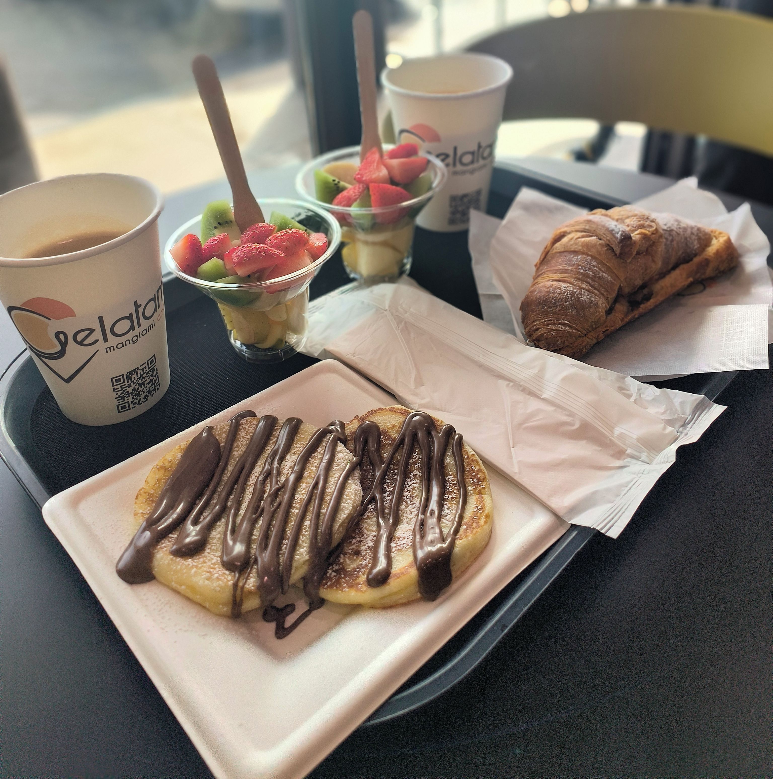 A tray with a chocolate-dipped pastry, a croissant, and a cup of coffee.
