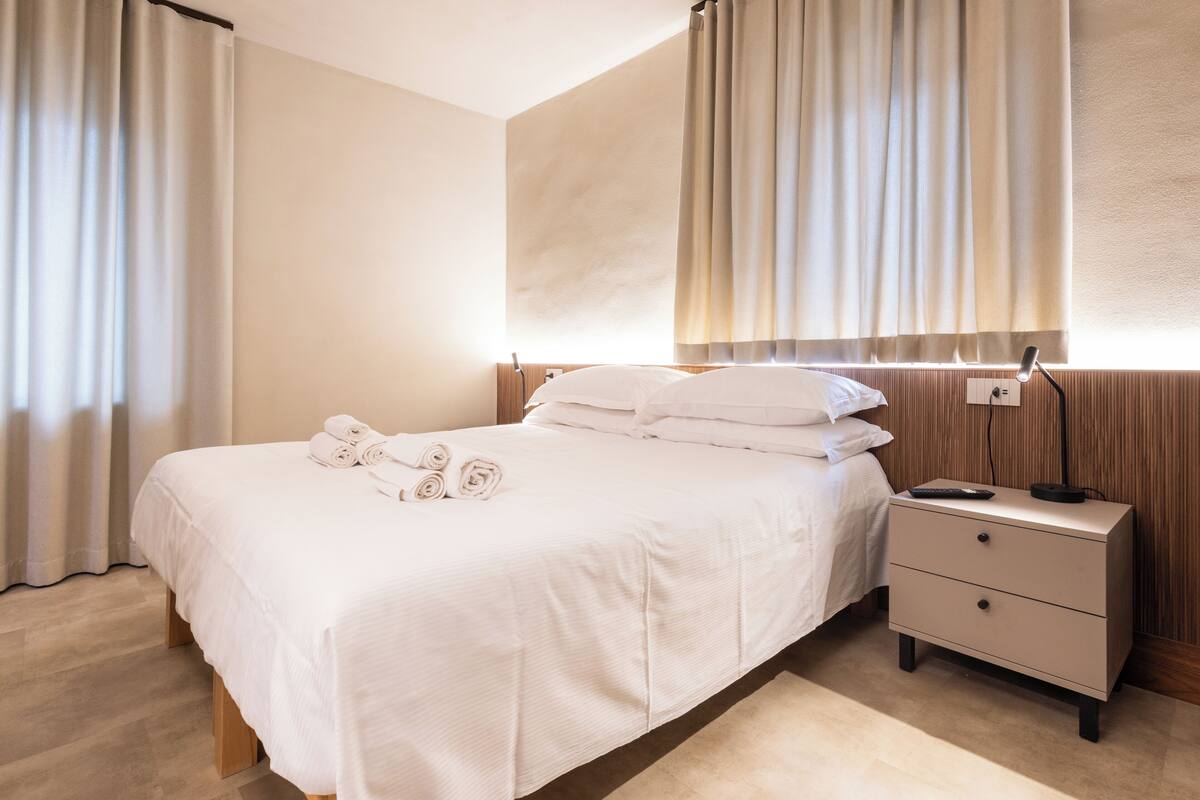 Un lit bien fait, avec des serviettes pliées, une table de chevet avec une lampe et une tête de lit en bois.