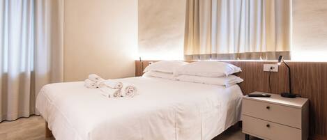 A neatly made bed with rolled towels, a bedside table with a lamp, and a wooden headboard.