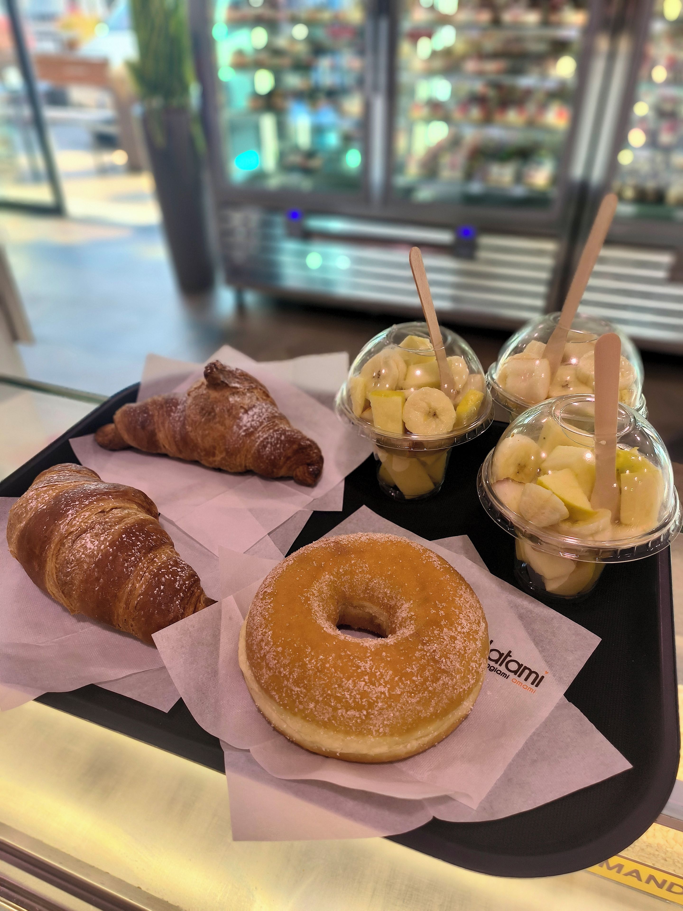 A tray with a croissant, a glazed donut, and two cups of fruit yogurt with wooden sticks.
