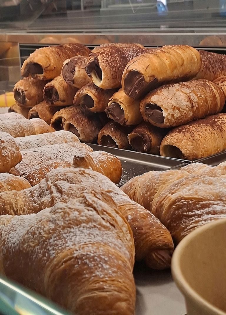Exposição de doces, incluindo croissants e doces recheados com chocolate, em uma padaria.