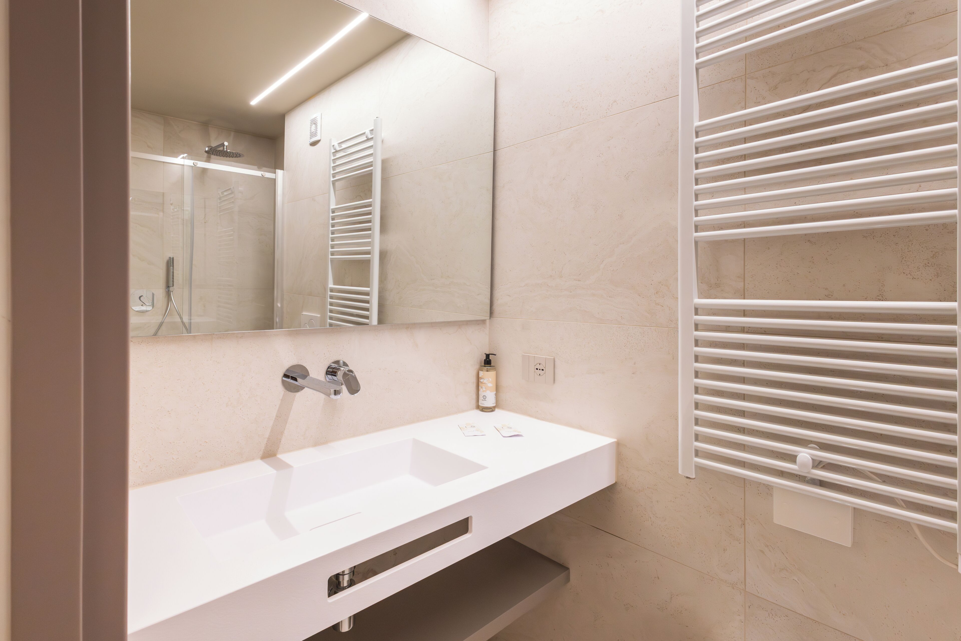 A modern bathroom with a white sink, a mirror, a towel rack, and a shower area.