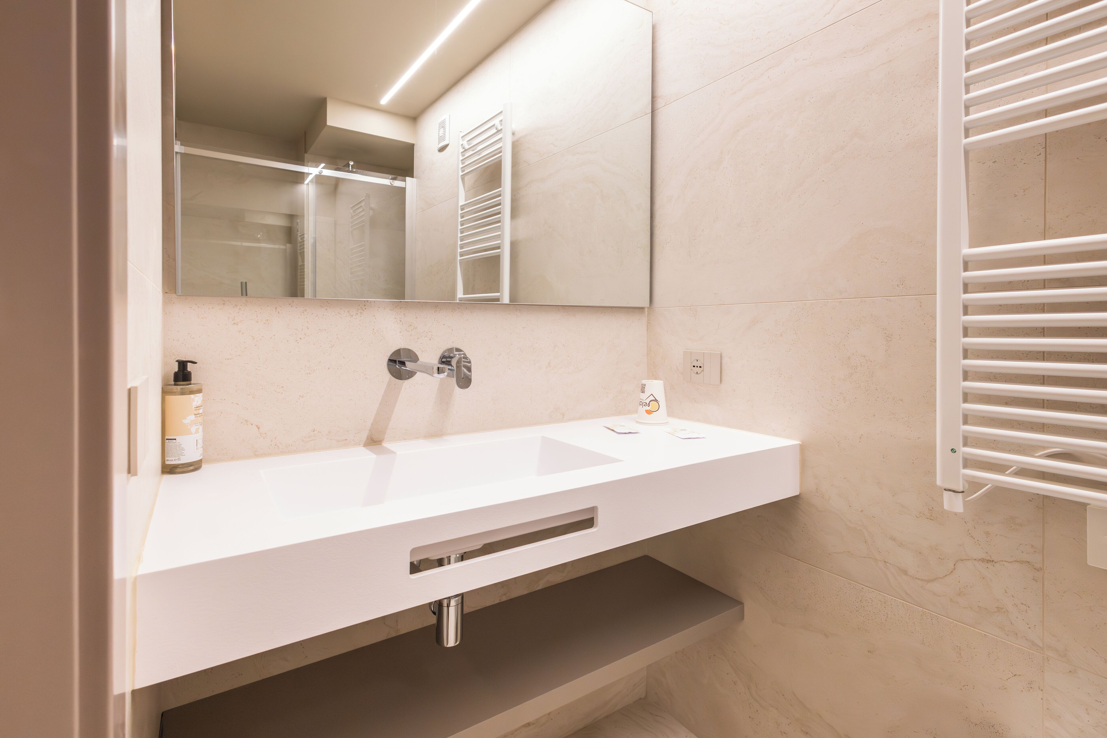 Un baño moderno con un lavamanos blanco, un espejo y un perchero para toallas.