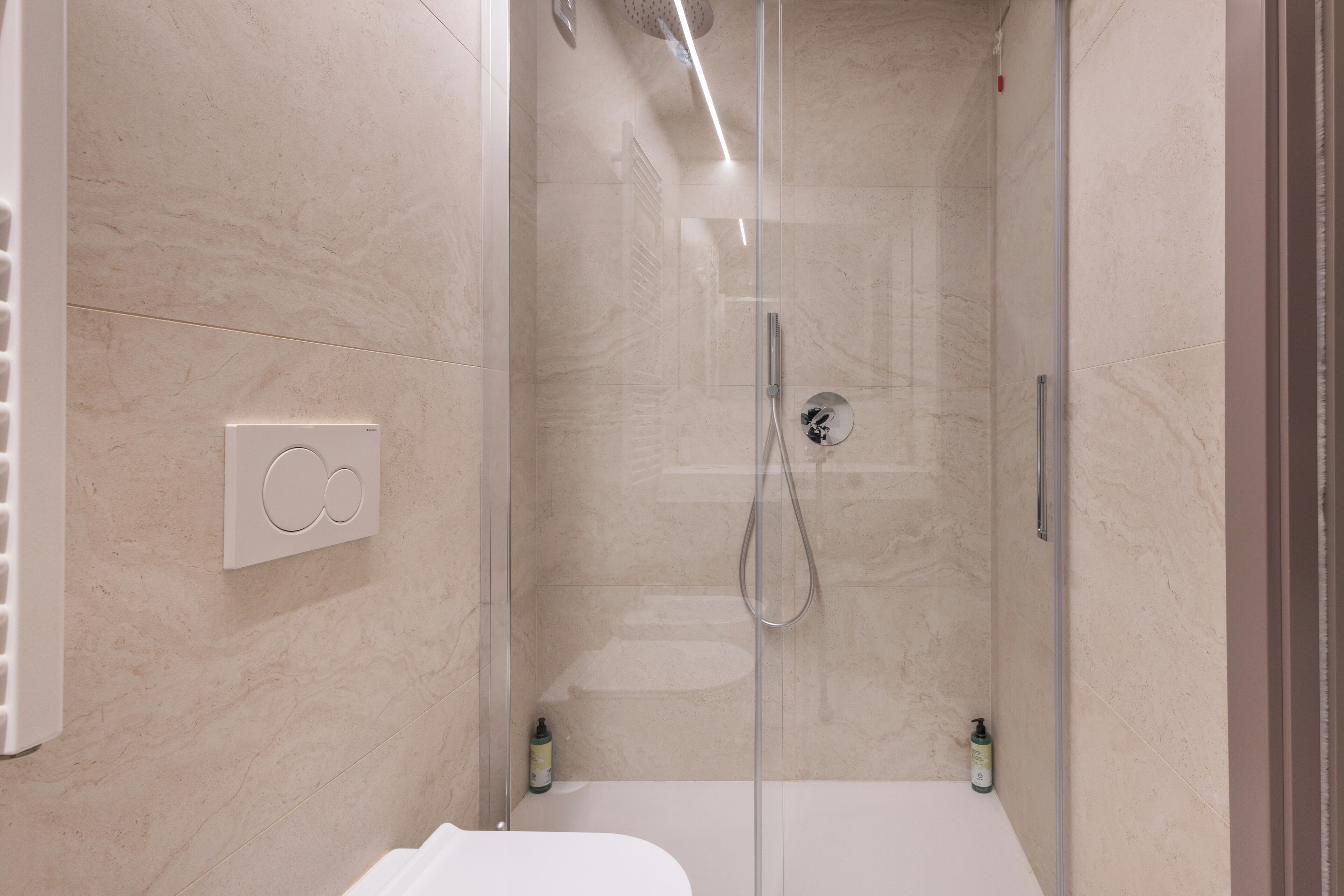Ein modernes Badezimmer mit einer glasumschlossenen Dusche, einer weißen Badewanne und einem Wandheizkörper.
