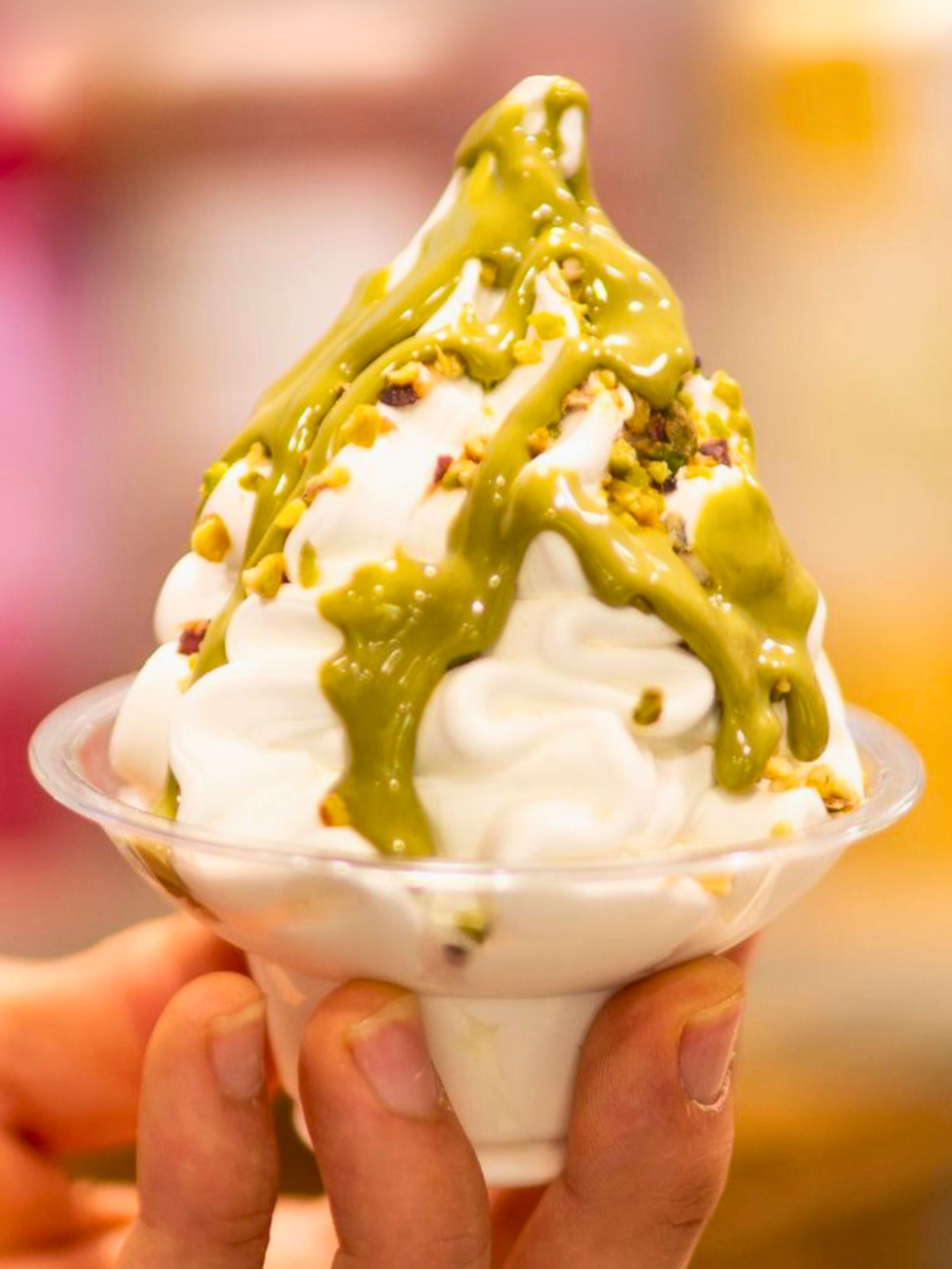 Una mano sosteniendo un tazón de hielo raspado cubierto de crema batida y un chorrito verde, probablemente un postre.