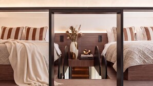 Una habitación de hotel moderna con una mesa central, dos camas con almohadillas a rayas y un jarrón con flores secas.