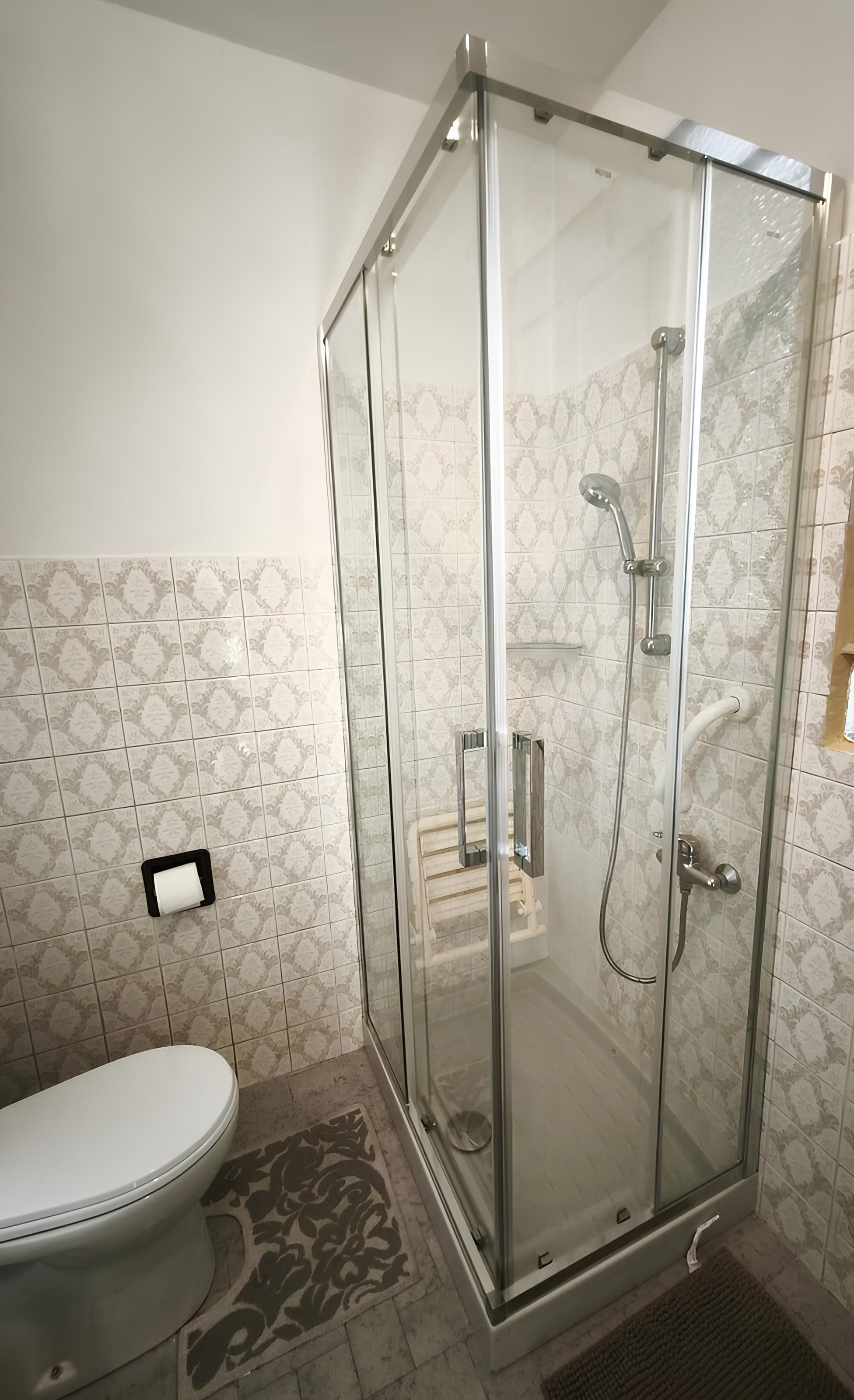 A modern bathroom with a glass-enclosed shower, a toilet, and patterned tiles.
