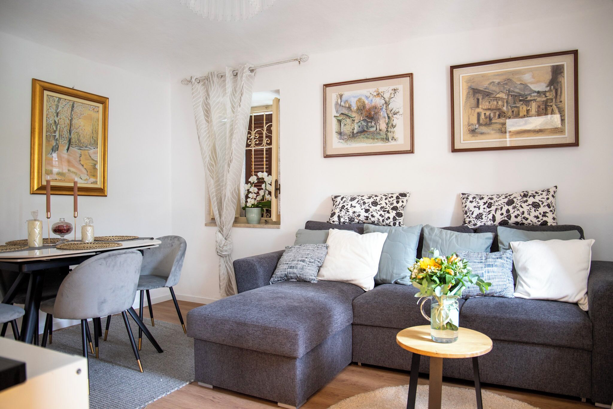 Una sala de estar con un sofá gris, una mesa de comedor con sillas y cuadros en la pared.