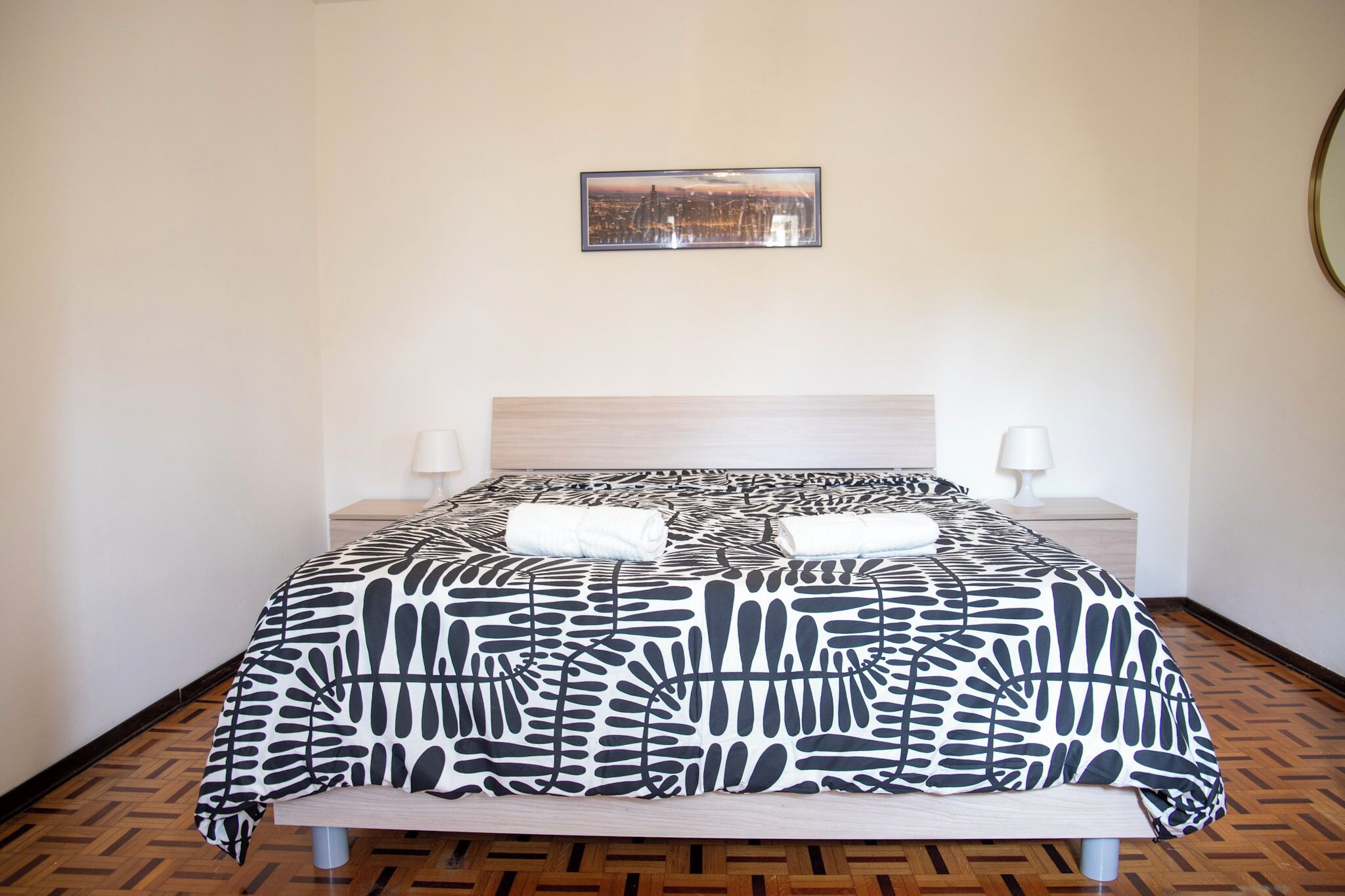 Una cama bien hecha con un edredón estampado, dos lámparas de noche y un cuadro en la pared.