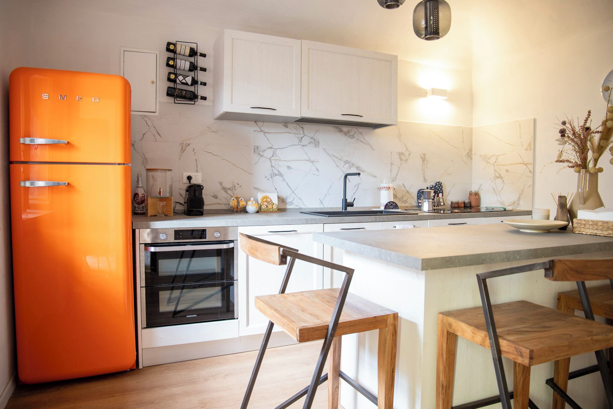 Una cocina moderna con armarios blancos, un salpicadero de mármol y un refrigerador naranja brillante.