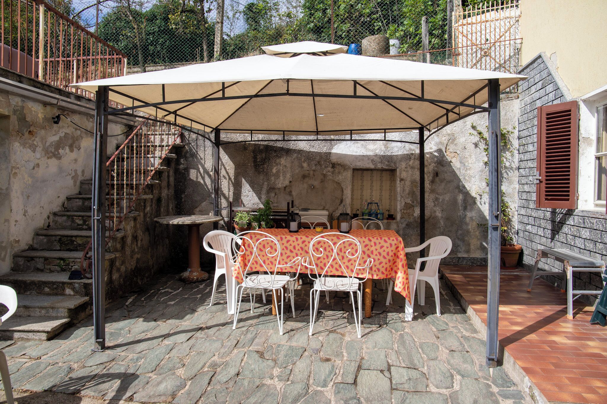 A covered outdoor patio with a table and chairs, stone steps, and a staircase.