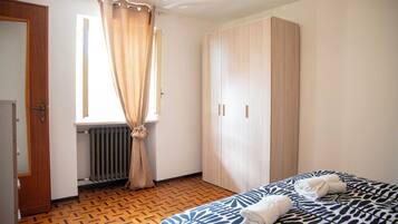 Ein Schlafzimmer mit Bett, Kleiderschrank, Heizkörper und einem Fenster mit Vorhängen.