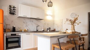 A modern kitchen with white cabinets, a marble backsplash, a built-in oven, and a central island with bar stools. - Ca' Dij Noni (Valle San Nicolao)