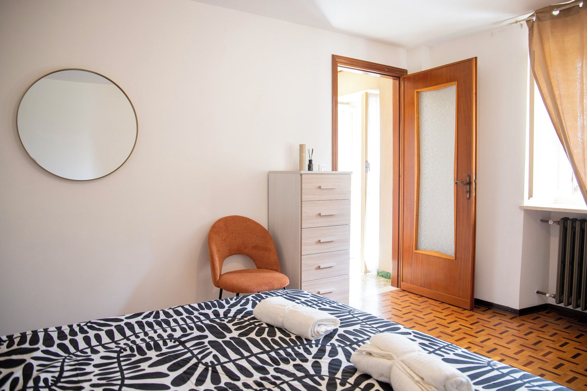 Quarto com cama, uma cadeira, cômoda e porta que dá para outro espaço.